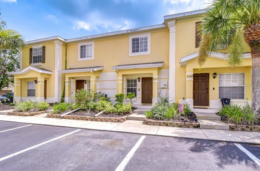 A row of yellow two-story townhomes with brown doors and a paved parking lot — 8551 TRAIL WIND DRIVE, TAMPA, FL