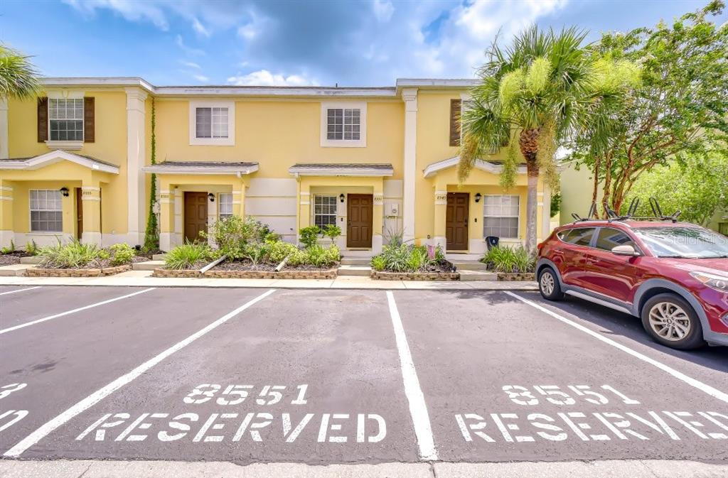 A row of yellow townhouses features reserved parking spaces in the foreground — 8551 TRAIL WIND DRIVE, TAMPA, FL