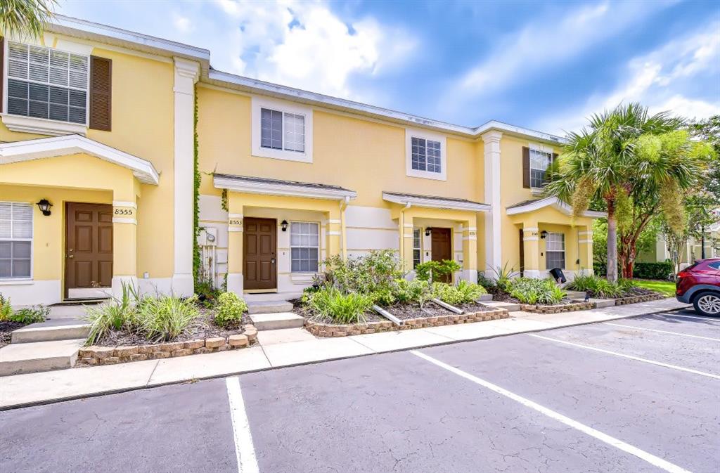 A row of yellow townhouses with brown doors and a parking lot in front — 8551 TRAIL WIND DRIVE, TAMPA, FL