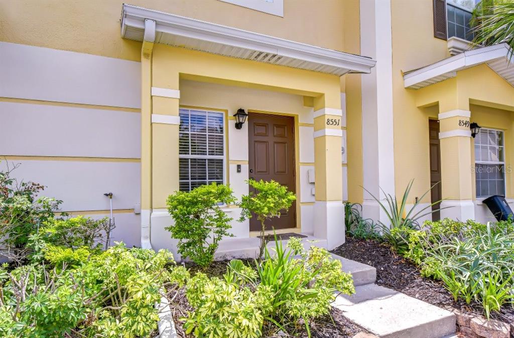 The exterior of a yellow townhouse features a covered entryway with a brown front door — 8551 TRAIL WIND DRIVE, TAMPA, FL