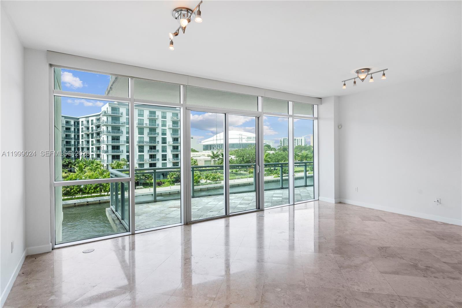 An empty living room features marble floors, floor-to-ceiling windows, and a balcony overlooking water — 1090 NW N River Dr # 402, Miami FL 33136, MIAMI, FL