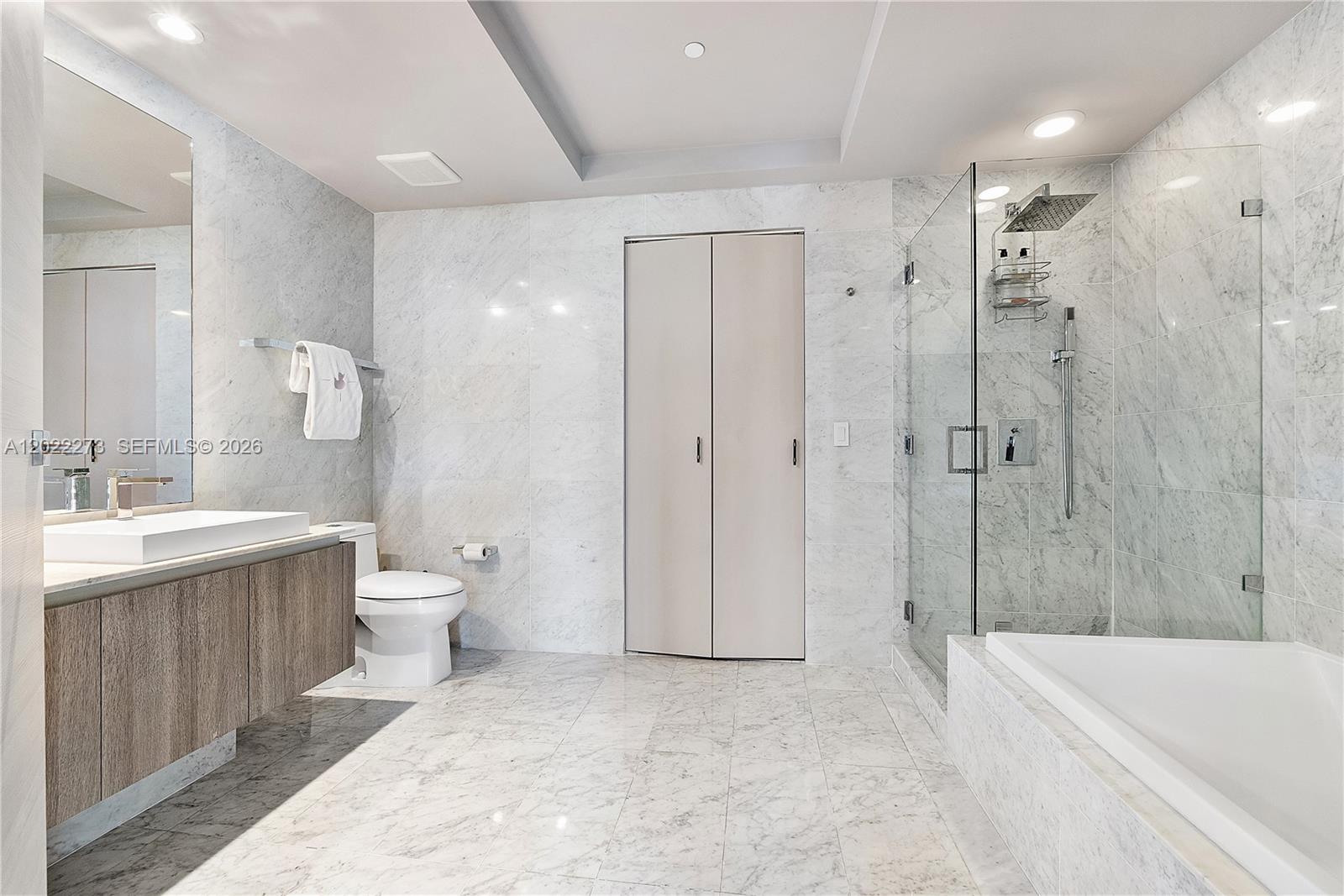 A modern bathroom features marble walls, a glass shower, a soaking tub, and wood cabinetry — 801 S Miami Ave # 1004, Miami FL 33130, MIAMI, FL