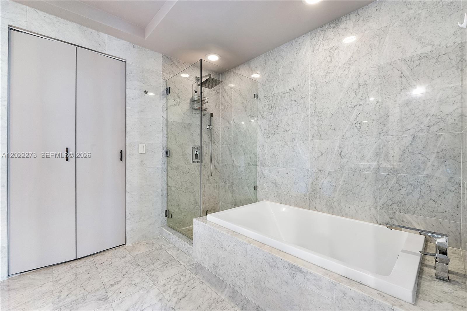 A bathroom features a glass-enclosed shower, a built-in bathtub, and marble tile finishes — 801 S Miami Ave # 1004, Miami FL 33130, MIAMI, FL