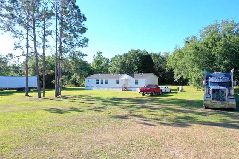 A single-story manufactured home sits on a large grassy lot with two semi-trucks parked nearby — 31326 TYNDALL ROAD, WESLEY CHAPEL, FL