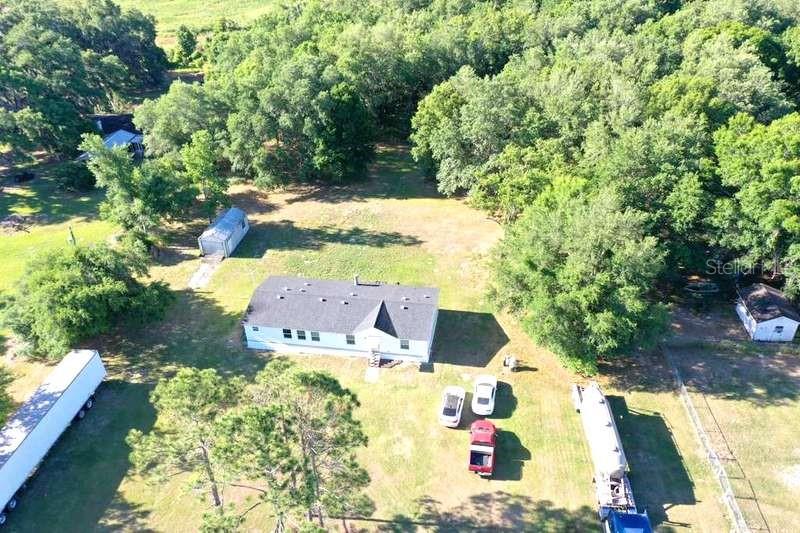 An aerial view shows a house, several outbuildings, and vehicles on a large, wooded lot — 31326 TYNDALL ROAD, WESLEY CHAPEL, FL
