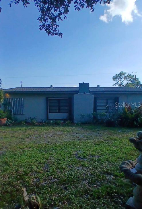 A single-story house with a central chimney and a large front yard under a blue sky — 1286 SW TROPICAL TERRACE, STUART, FL