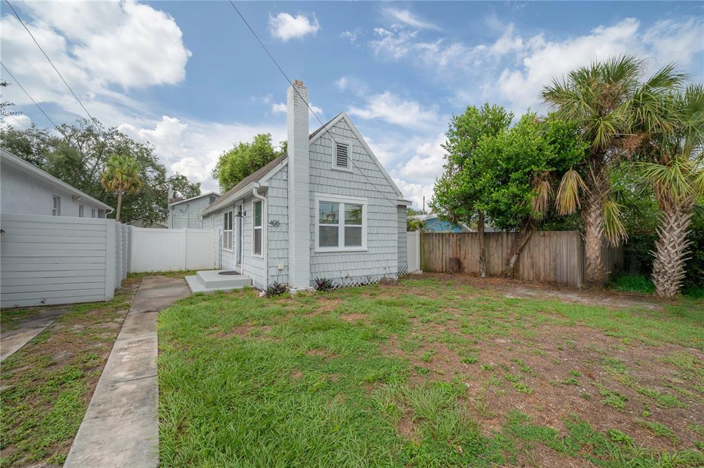 A light blue cottage with a chimney stands behind a grassy yard and wooden fence — 405 E CAYUGA STREET, TAMPA, FL