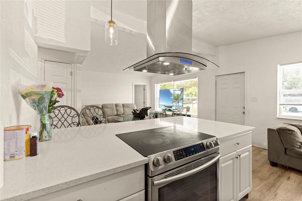 A kitchen island with a glass-top stove and stainless steel hood overlooks a living area — 4821 ELFRIDA AVENUE, SARASOTA, FL