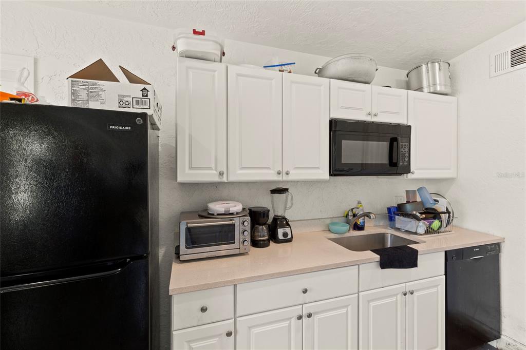 A kitchen features white cabinets, a black refrigerator, a microwave, and a stainless steel sink — 4821 ELFRIDA AVENUE, SARASOTA, FL