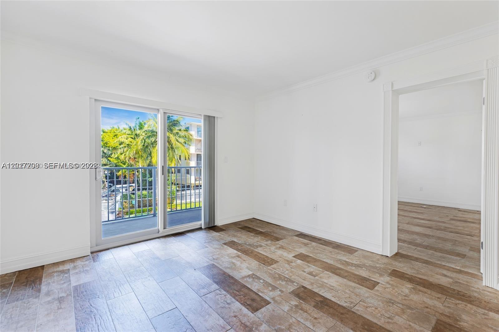 An empty room features wood-look tile flooring, white walls, and a sliding glass balcony door — 1674 Bay Rd # 302, Miami Beach FL 33139, MIAMI BEACH, FL