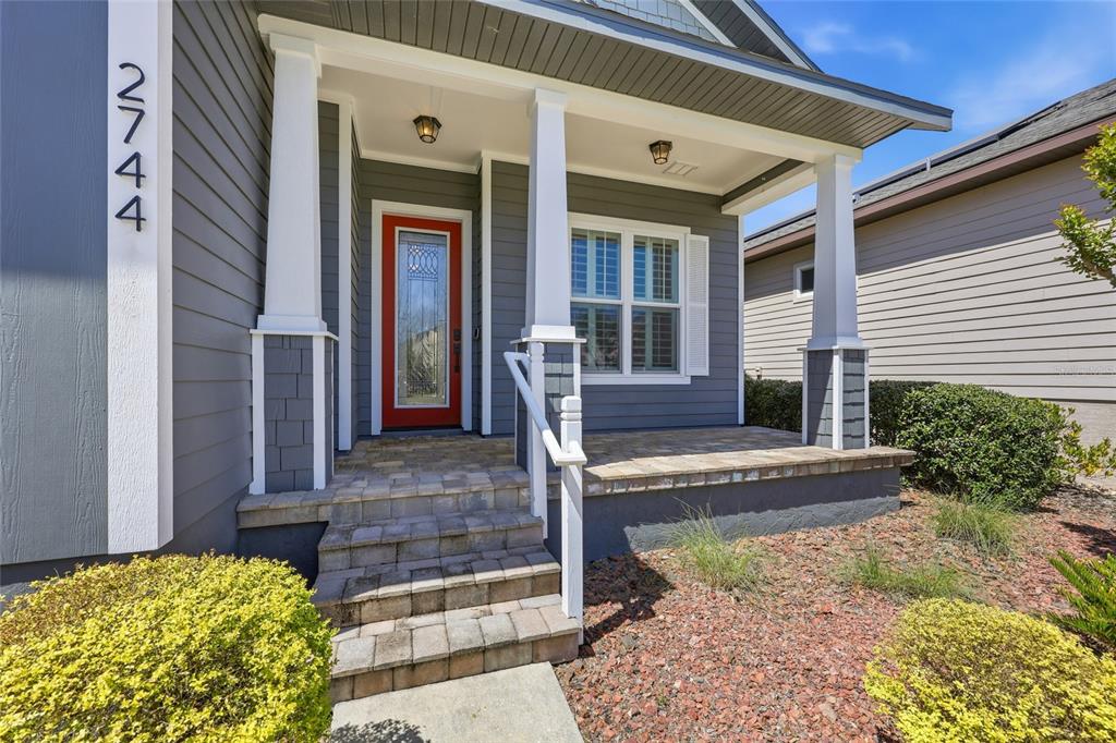 A gray house exterior features a red front door, a covered porch, and stone steps — 2744 SW 118TH TERRACE, GAINESVILLE, FL