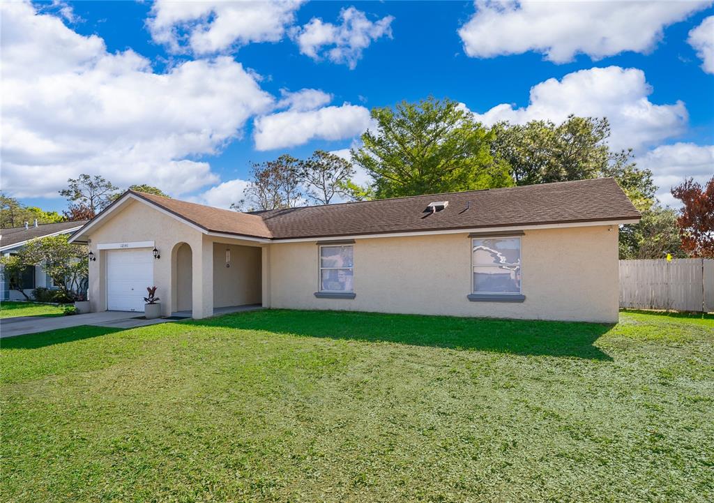 A single-story house with a beige stucco exterior, a brown shingled roof, and a garage — 12141 CAPER STREET, ORLANDO, FL