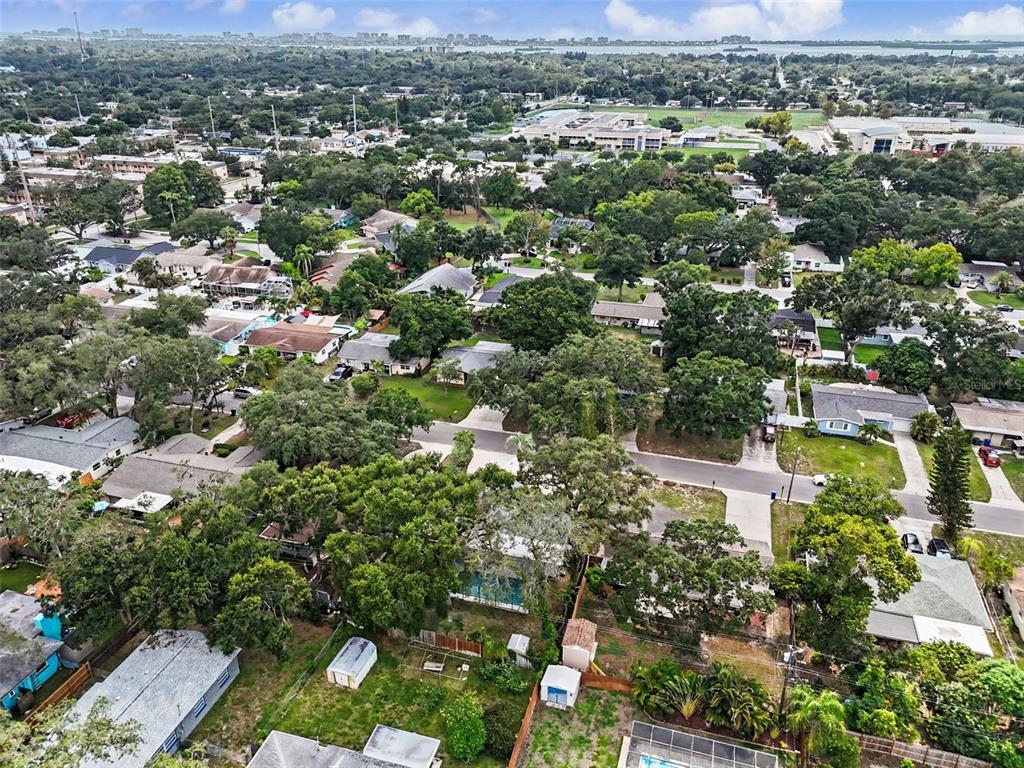An aerial view shows a suburban neighborhood with many trees, houses, and a school nearby — 57 VENTURA DRIVE, DUNEDIN, FL