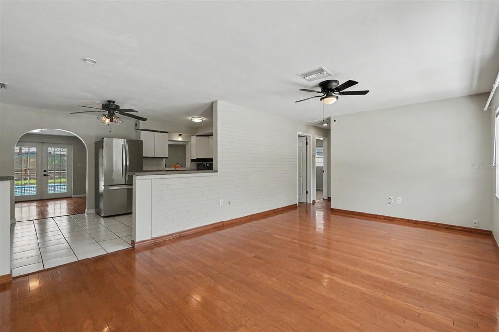 A living room with hardwood floors, a white brick half-wall, and an adjacent kitchen — 57 VENTURA DRIVE, DUNEDIN, FL