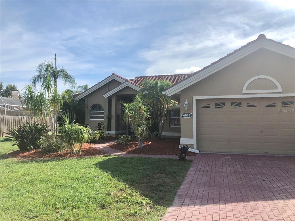 A single-story house with a tan stucco exterior, a tile roof, and a brick driveway — 4011 72ND AVENUE E, SARASOTA, FL