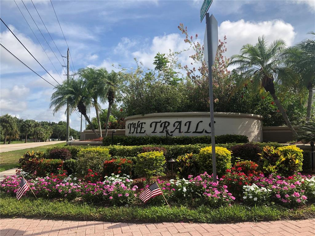 A stone monument sign for The Trails sits in a landscaped garden with American flags — 4011 72ND AVENUE E, SARASOTA, FL