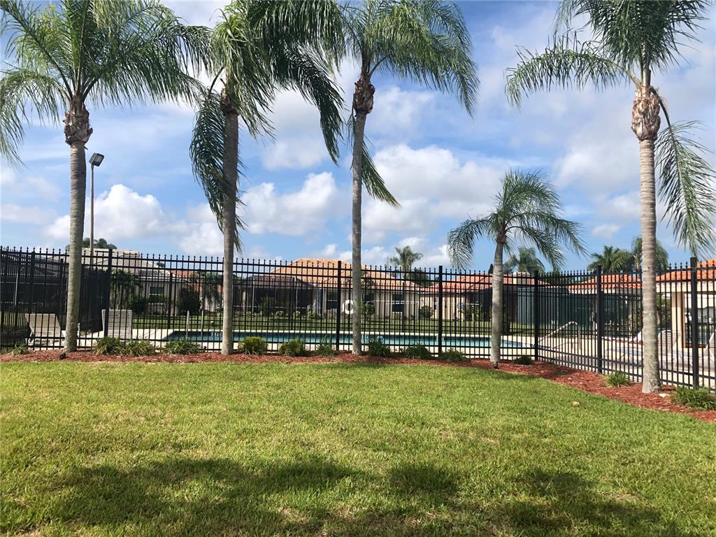 A black metal fence encloses a swimming pool area with palm trees and green grass — 4011 72ND AVENUE E, SARASOTA, FL