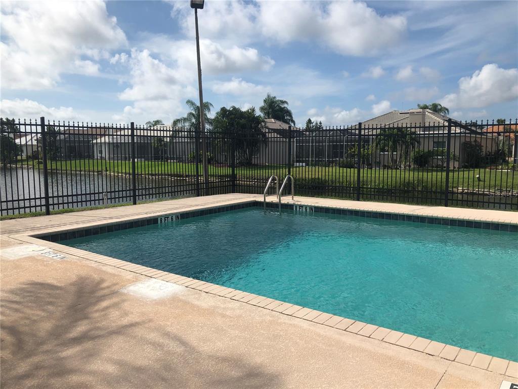 A rectangular swimming pool with a metal fence sits in front of a residential lake — 4011 72ND AVENUE E, SARASOTA, FL