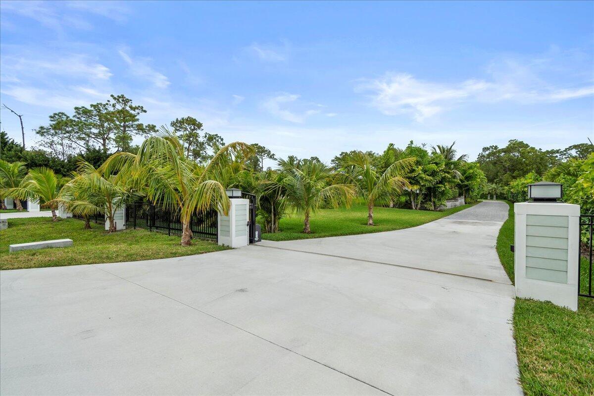 A concrete driveway leads through a gated entrance into a lush, palm-filled residential yard — 12875 157th Street N, Jupiter FL 33478, JUPITER, FL