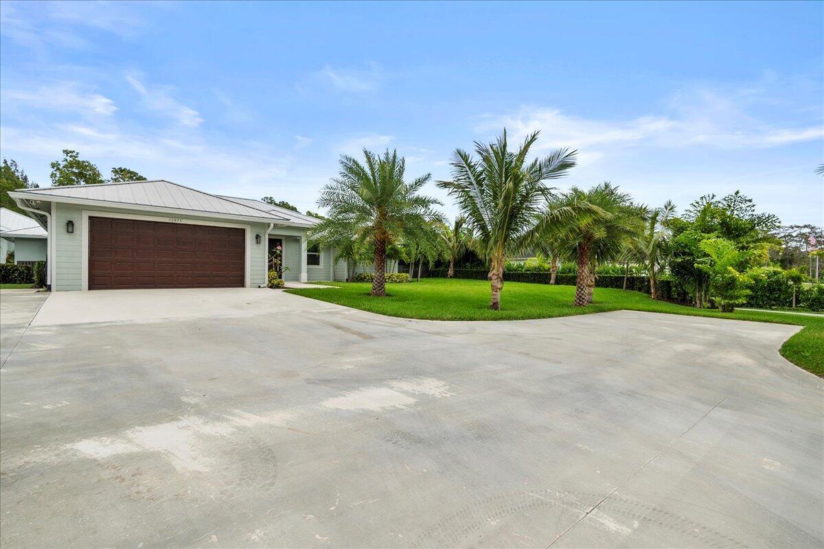 A light-colored house with a metal roof and a large concrete driveway with palm trees — 12875 157th Street N, Jupiter FL 33478, JUPITER, FL