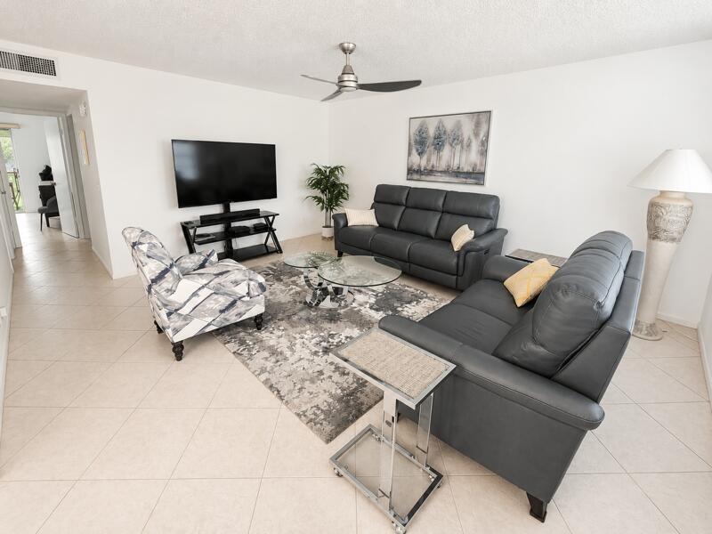 A living room features two dark leather sofas, a patterned armchair, and a glass coffee table — 567 Burgundy L, Delray Beach FL 33484, DELRAY BEACH, FL