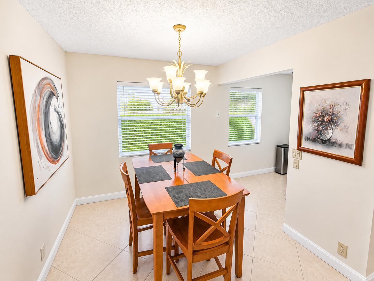 A dining room features a wooden table with four chairs, a chandelier, and two wall paintings — 567 Burgundy L, Delray Beach FL 33484, DELRAY BEACH, FL