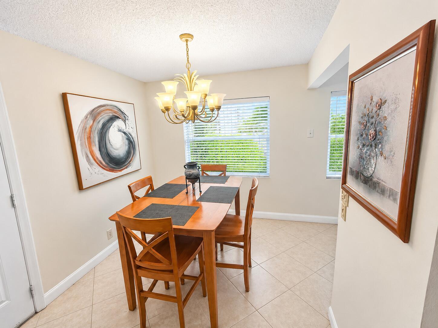 A dining room features a wooden table with four chairs, a chandelier, and two wall paintings — 567 Burgundy L, Delray Beach FL 33484, DELRAY BEACH, FL