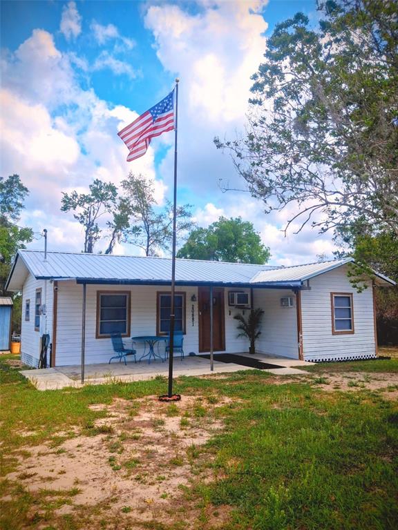 A white single-story house with a metal roof and an American flag on a pole — 20881 SE 142ND PLACE, UMATILLA, FL