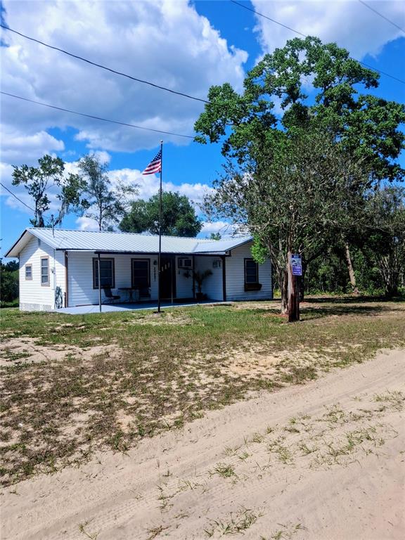 A single-story white house with a metal roof and an American flag in the yard — 20881 SE 142ND PLACE, UMATILLA, FL