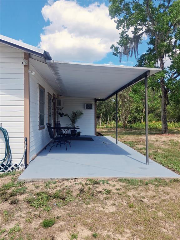 A covered concrete patio extends from the side of a white house with a metal roof — 20881 SE 142ND PLACE, UMATILLA, FL