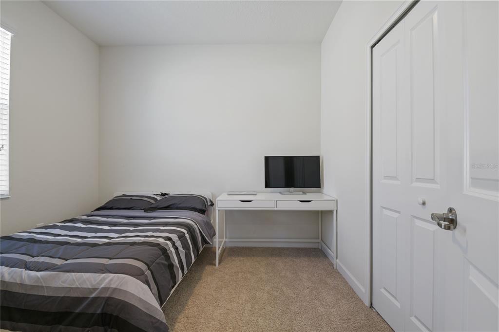 A bedroom features a bed with striped bedding, a white desk, and a closet door — 2157 LAKE SIDE AVENUE, DAVENPORT, FL