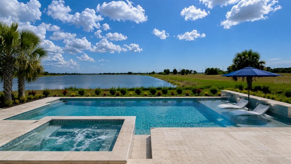 An infinity pool and spa overlook a lake under a blue sky with clouds — 44 SUNFLOWER DRIVE, PLACIDA, FL
