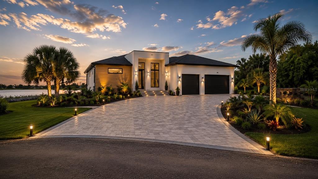 A modern single-story house with a paved driveway, palm trees, and a waterfront view at sunset — 44 SUNFLOWER DRIVE, PLACIDA, FL