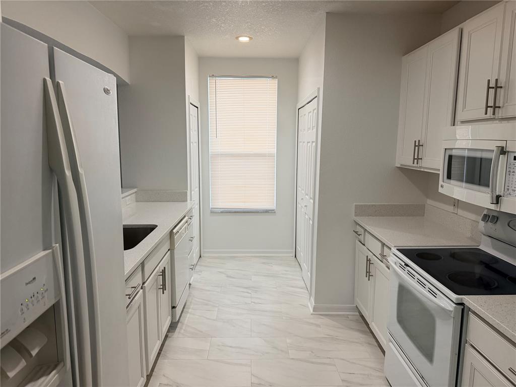 A galley kitchen features white cabinets, light countertops, stainless steel appliances, and marble-look tile flooring — 642 CAPTIVA CIRCLE UNIT 642, KISSIMMEE, FL