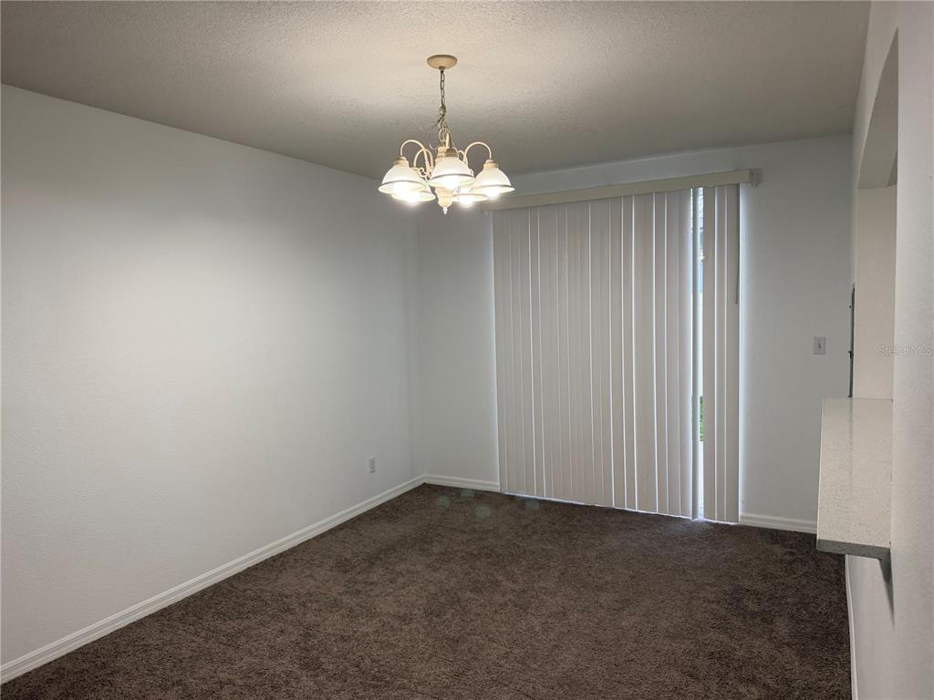 A dining area with brown carpet, white walls, a chandelier, and vertical blinds on a door — 642 CAPTIVA CIRCLE UNIT 642, KISSIMMEE, FL