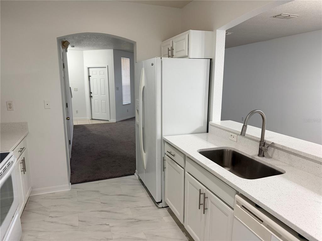 A kitchen with white cabinets, quartz countertops, and a stainless steel sink overlooks a carpeted room — 642 CAPTIVA CIRCLE UNIT 642, KISSIMMEE, FL