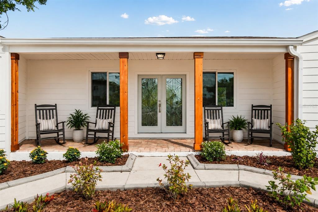 A covered front porch features four rocking chairs, wood columns, and a double glass door — 7745 WESTMORELAND DRIVE, SARASOTA, FL