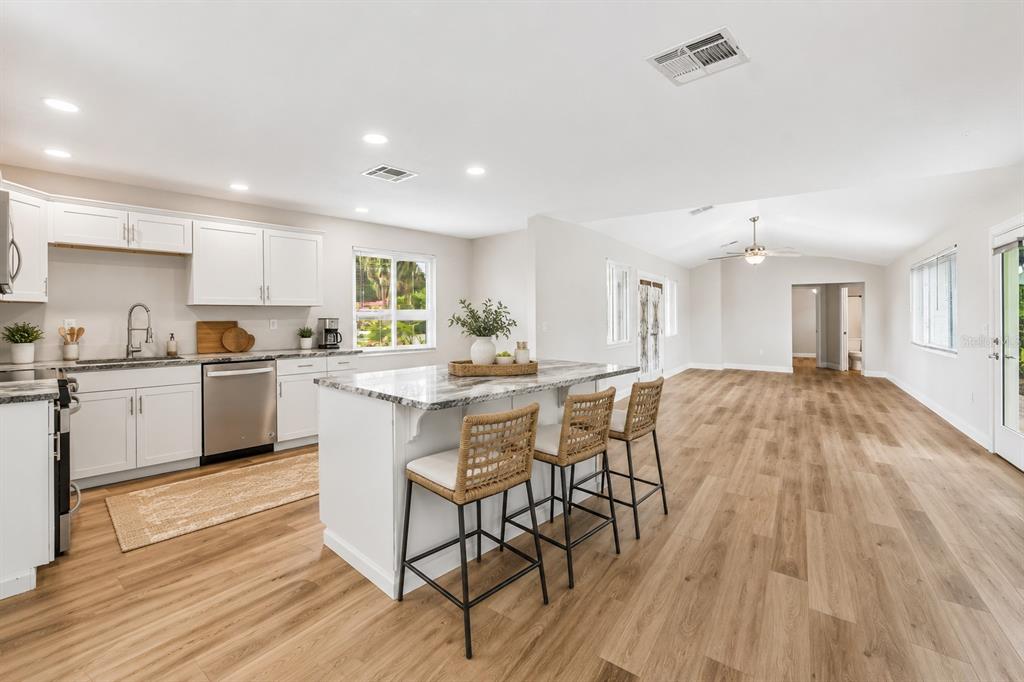 A kitchen with white cabinets, a granite-topped island, and bar stools opens to a living area — 7745 WESTMORELAND DRIVE, SARASOTA, FL