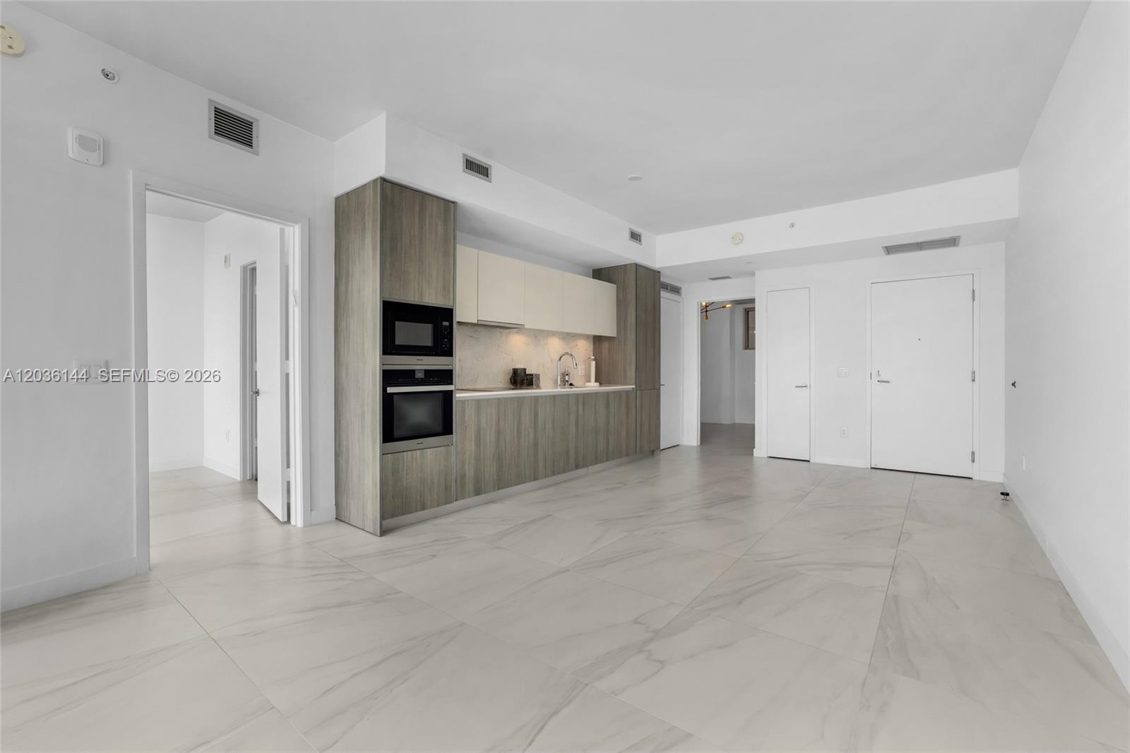 A modern kitchen with wood-grain cabinetry and white marble-style tile flooring in an open room — 2900 NE 7th Ave # 1806, Miami FL 33137, MIAMI, FL