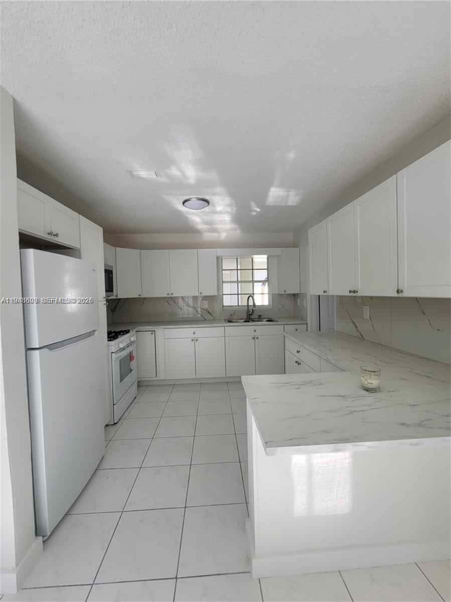 A white kitchen features marble-patterned countertops, white cabinetry, and light-colored tile flooring — 12305 SW 42nd St, Miami FL 33175, MIAMI, FL