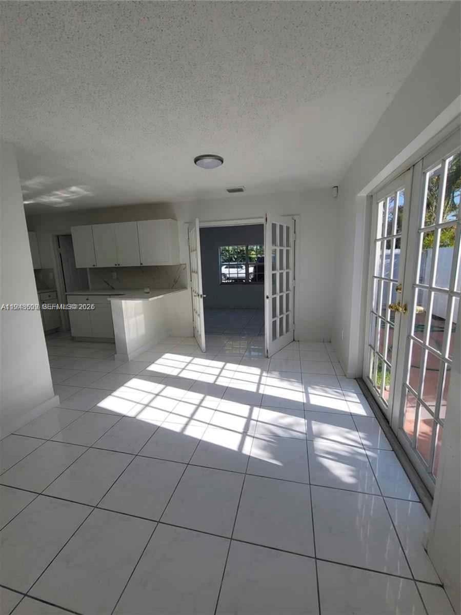 A bright room features white tile flooring, a kitchen area, and glass French doors — 12305 SW 42nd St, Miami FL 33175, MIAMI, FL