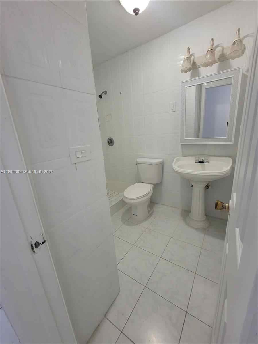 A small bathroom features white tile walls and floors, a pedestal sink, and a toilet — 12305 SW 42nd St, Miami FL 33175, MIAMI, FL