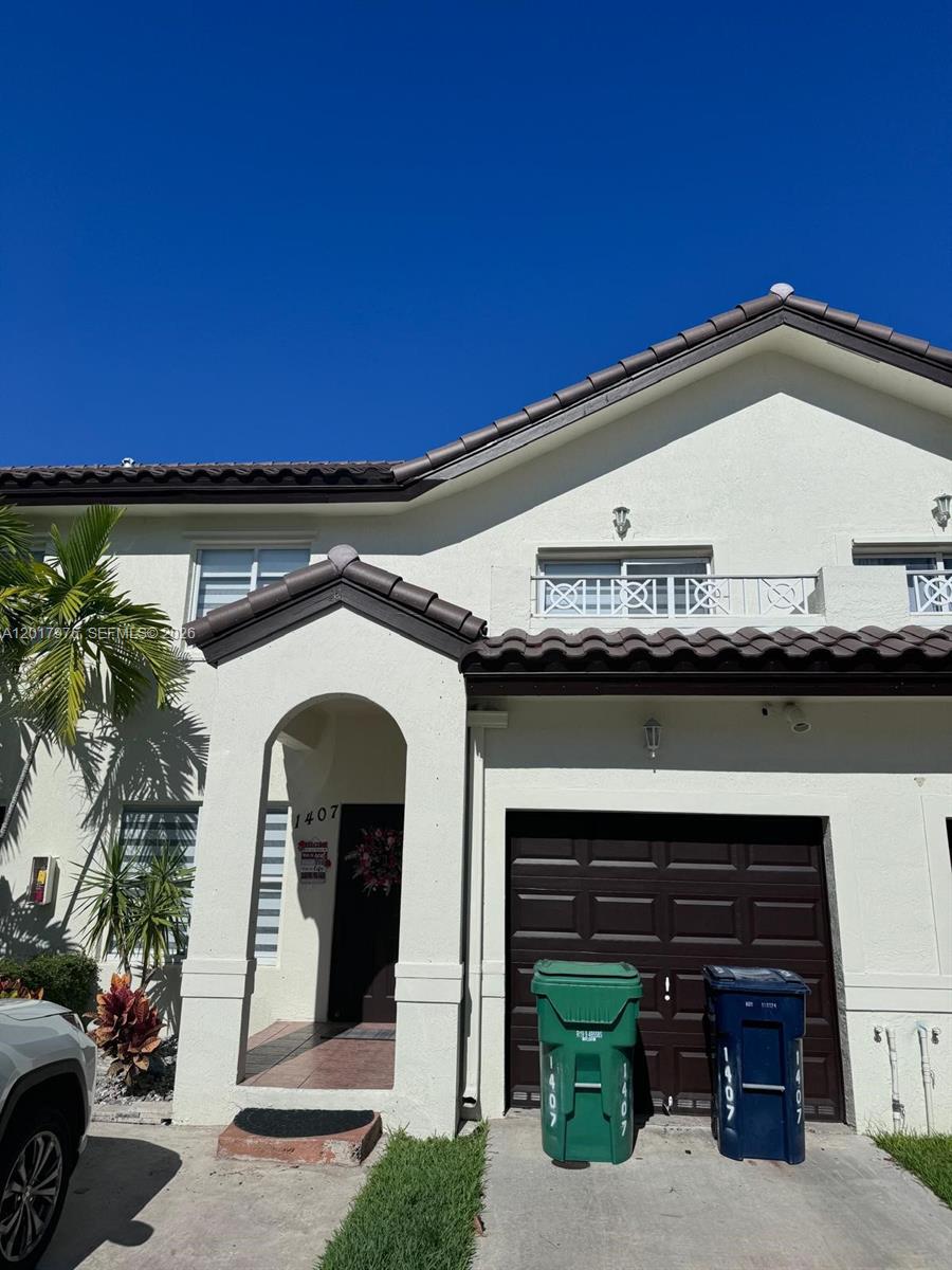 A two-story townhouse exterior features a brown garage door, arched entryway, and two trash bins — 8851 NW 110th Pl # 1407, Doral FL 33178, DORAL, FL