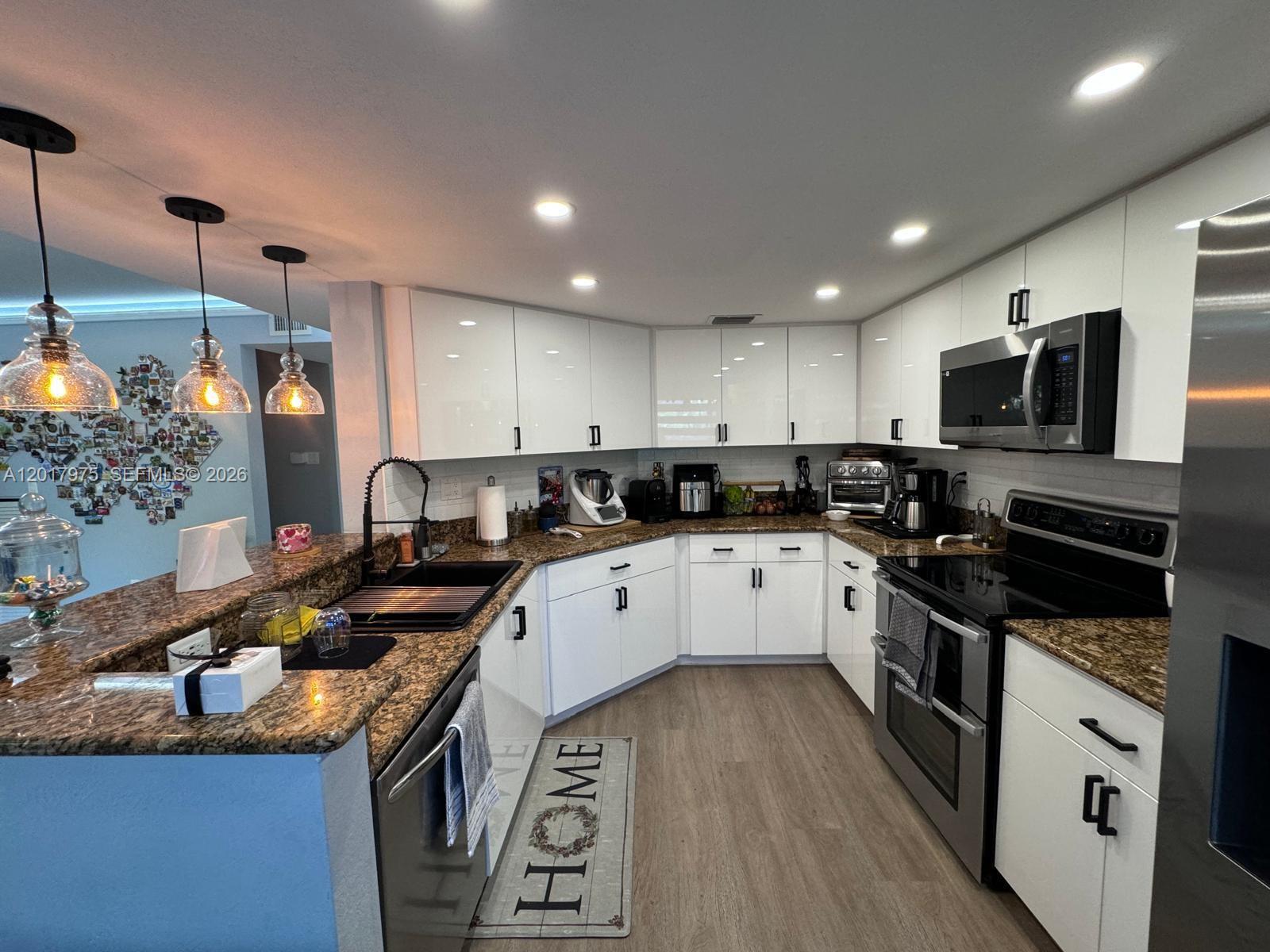A kitchen features white cabinets, granite countertops, stainless steel appliances, and three hanging pendant lights — 8851 NW 110th Pl # 1407, Doral FL 33178, DORAL, FL
