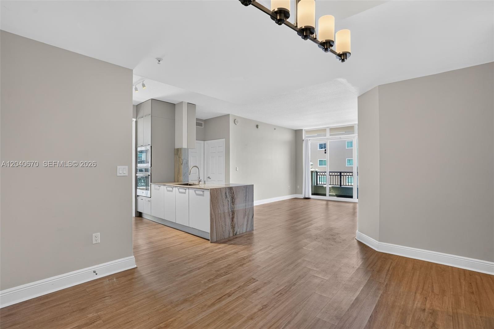 An open-concept kitchen with a stone-topped island overlooks a living area with wood flooring — 3232 SW 22nd Ter # 601, Miami FL 33145, MIAMI, FL