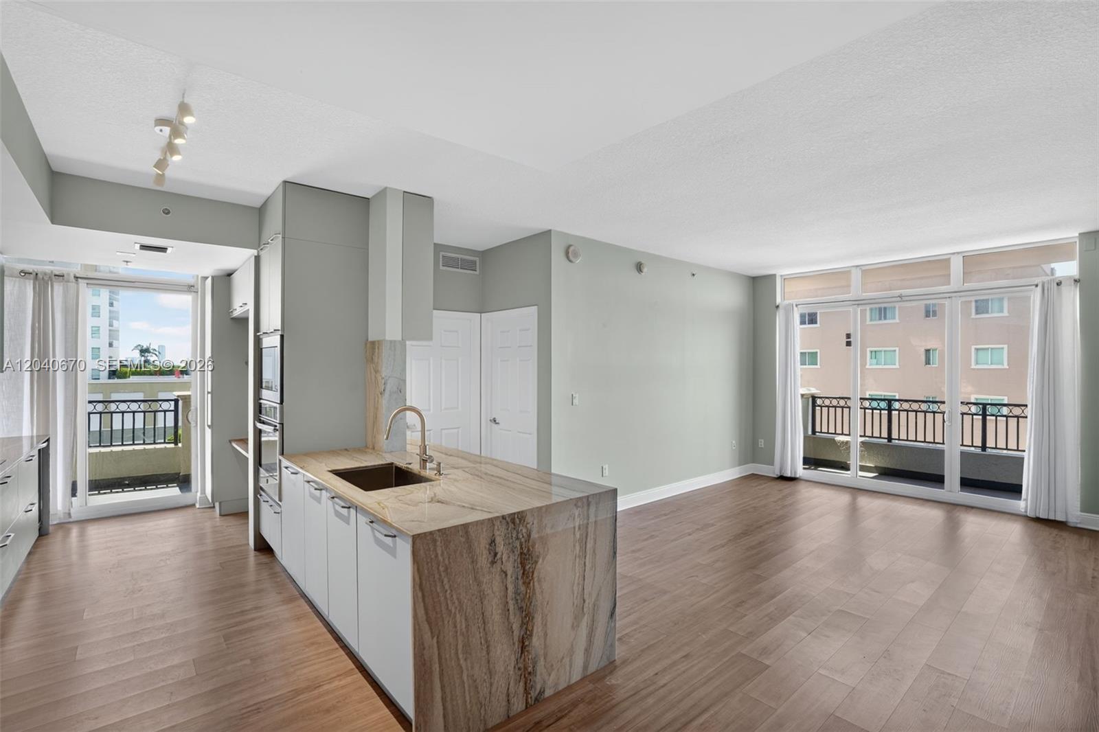 A modern kitchen with a stone island and wood floors opens to a living area — 3232 SW 22nd Ter # 601, Miami FL 33145, MIAMI, FL