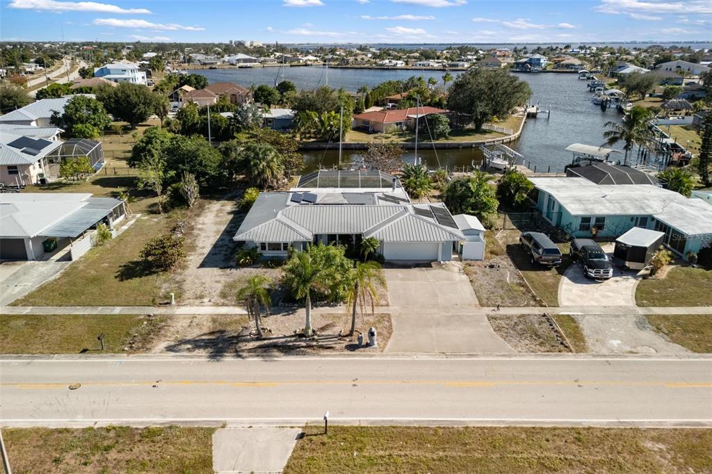 An aerial view shows a single-story house with a pool cage and a canal backyard — 105 COUSLEY DRIVE SE, PORT CHARLOTTE, FL