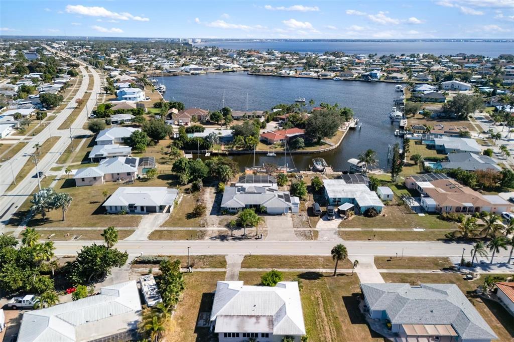 An aerial view shows waterfront houses with docks along a canal near a large bay — 105 COUSLEY DRIVE SE, PORT CHARLOTTE, FL