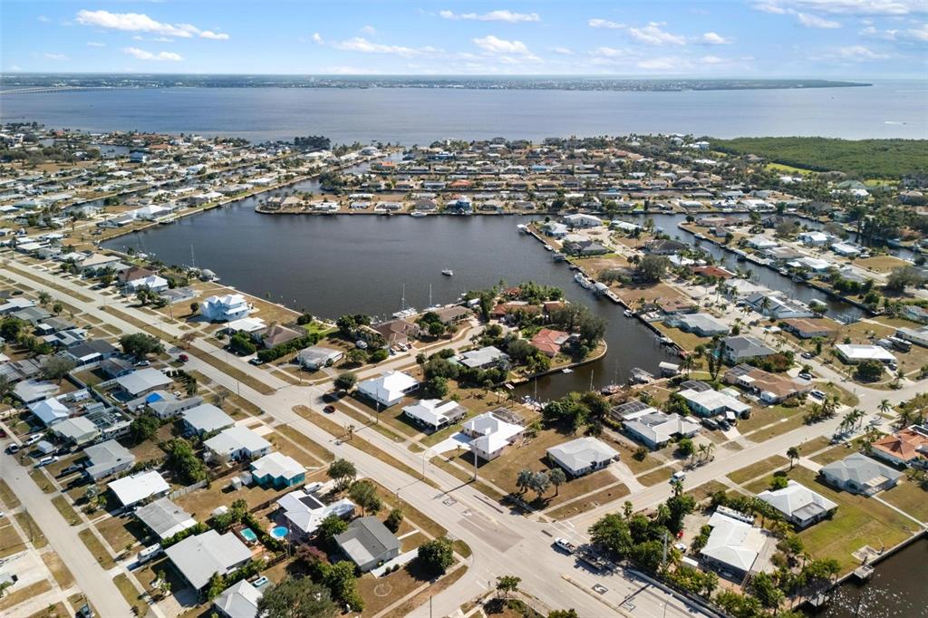An aerial view shows a residential neighborhood with canals and a large bay — 105 COUSLEY DRIVE SE, PORT CHARLOTTE, FL
