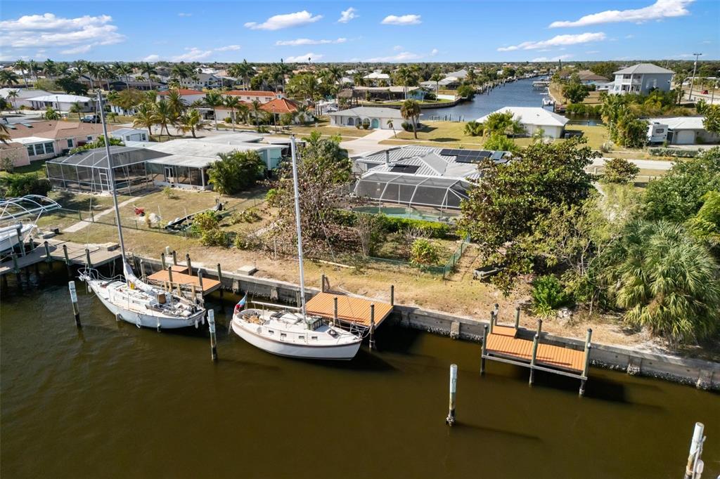 An aerial view shows two sailboats docked at a canal behind a residential property — 105 COUSLEY DRIVE SE, PORT CHARLOTTE, FL